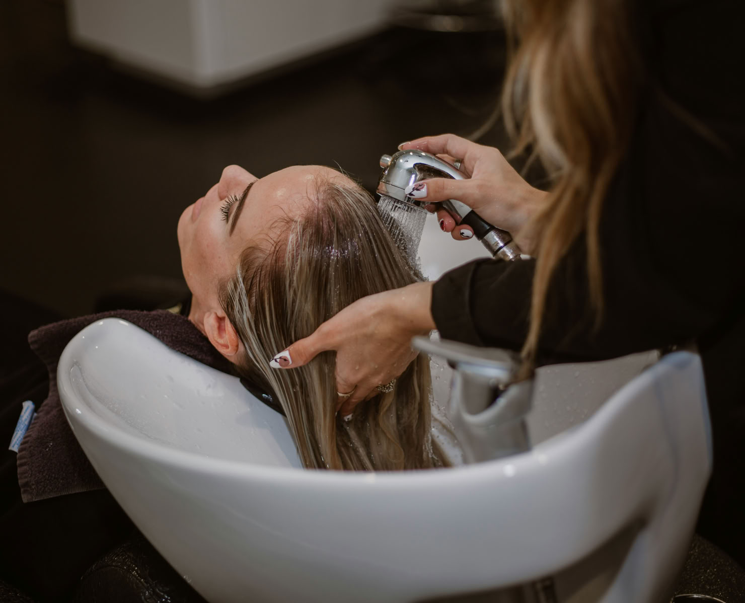A person getting their hair washed in a salon sink by a hairdresser.
